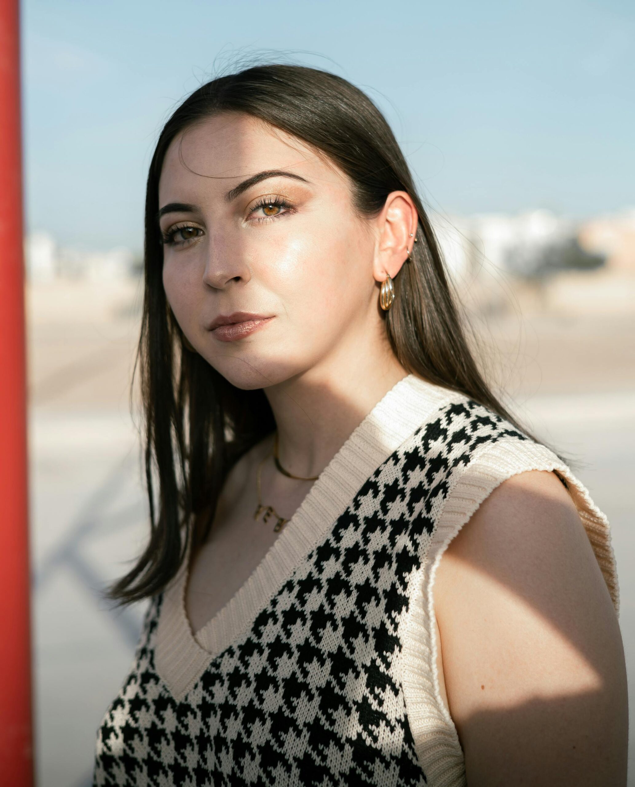 Outdoor portrait of a stylish young woman with gold jewelry in natural sunlight.